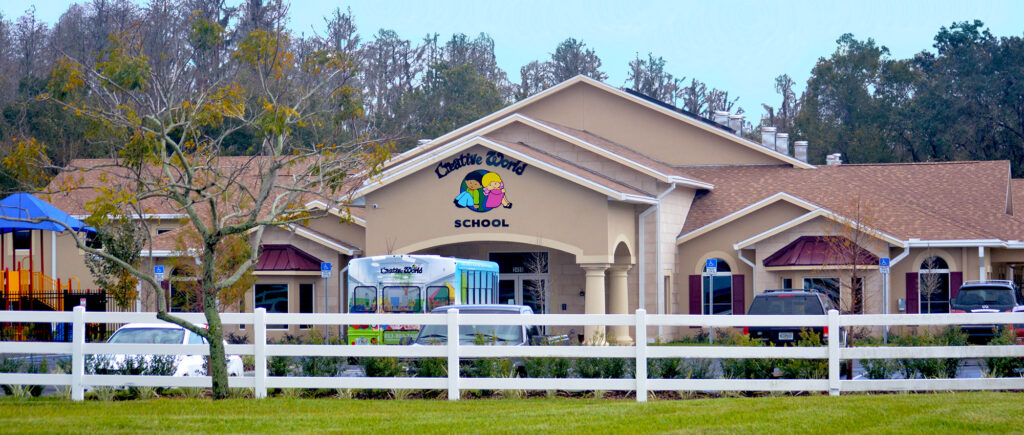 Front view of Creative World School at Oakstead, featuring the school building, branded bus, and a white fence.