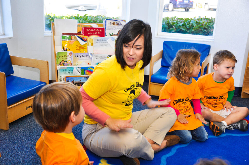 Teacher engaging with young children in a circle time activity at Creative World School, surrounded by colorful books and a cheerful classroom environment.