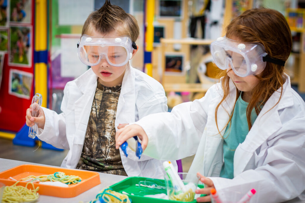 Children dressed as scientists conducting a fun hands-on experiment with colorful spaghetti at Creative World School.