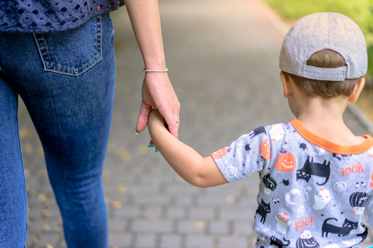 Woman walking hand in hand with a boy wearing a cap