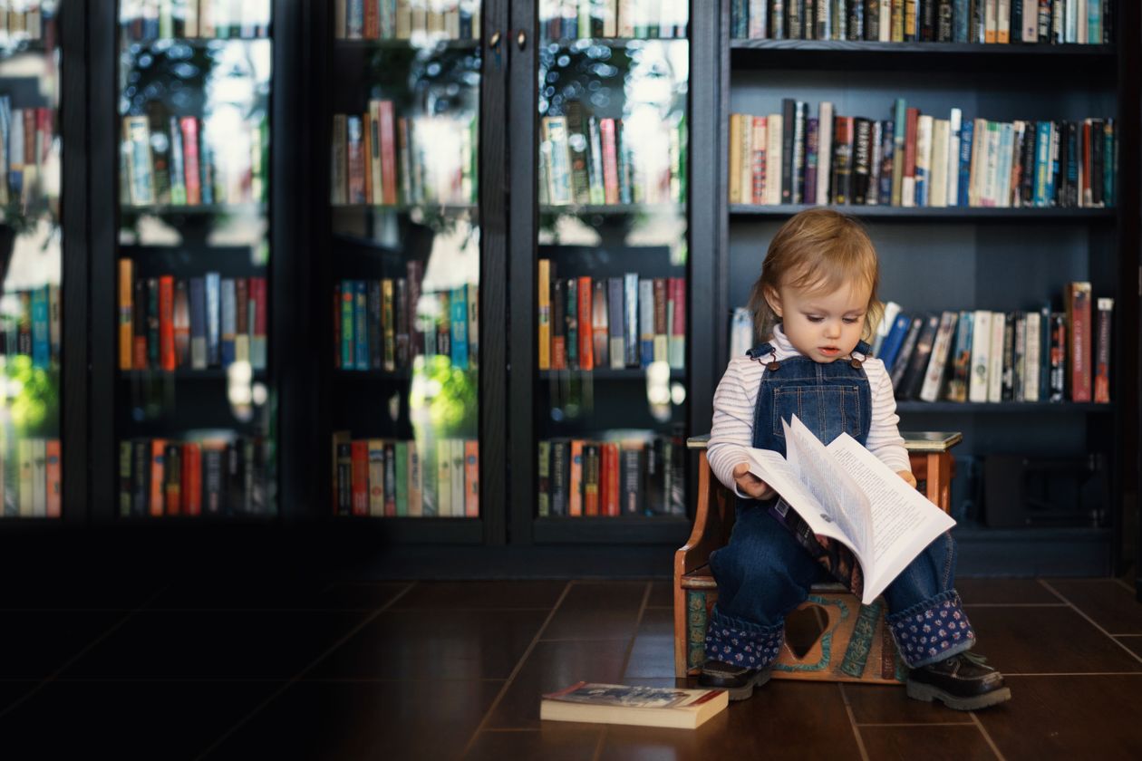 Toddler sitting on a wooden chair holding a book