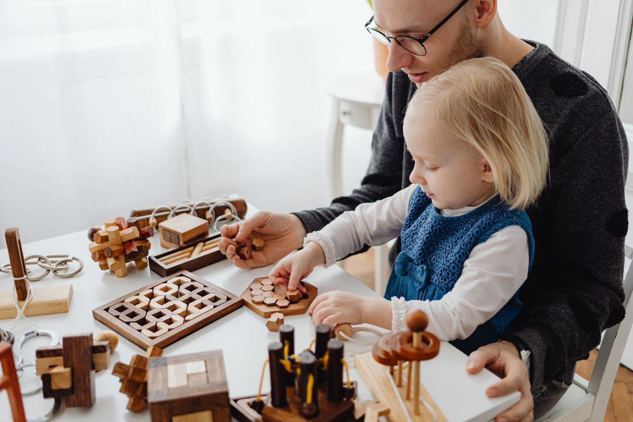 A young girl sitting on her father's lap while playing with wooden toys