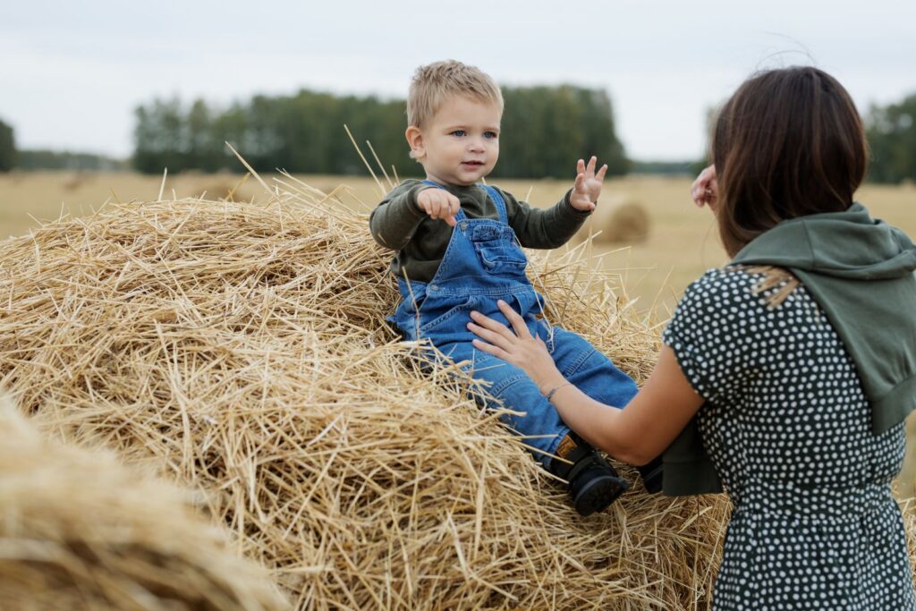 Toddler in overalls sitting on a hay bale in a fall field with his mom near Franklin Township