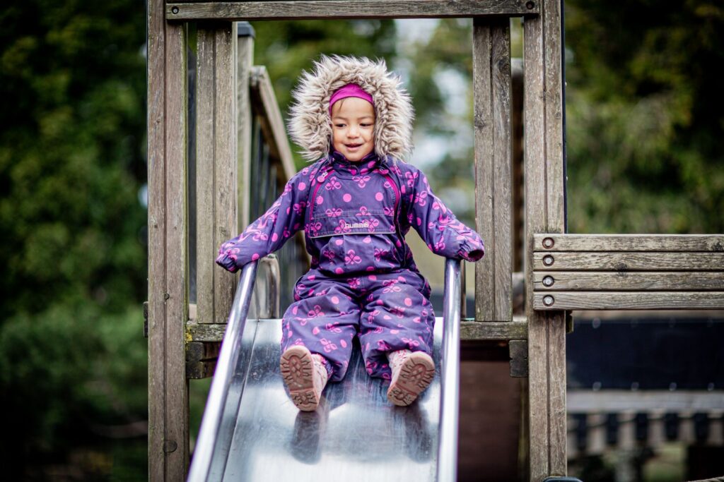 Preschooler in a purple jacket at the top of a playground slide on a cool fall afternoon