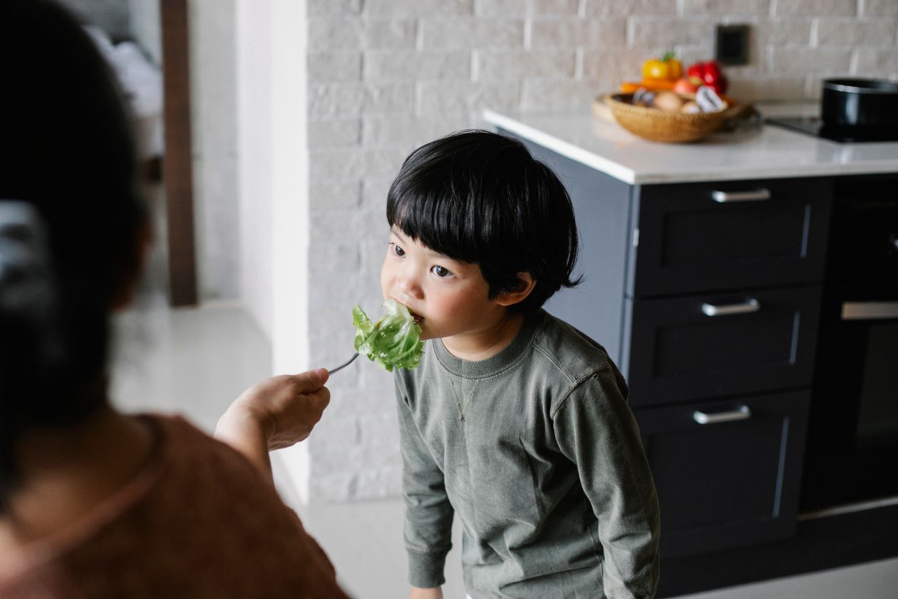 Ethnic mother feeding little son with salad leaves