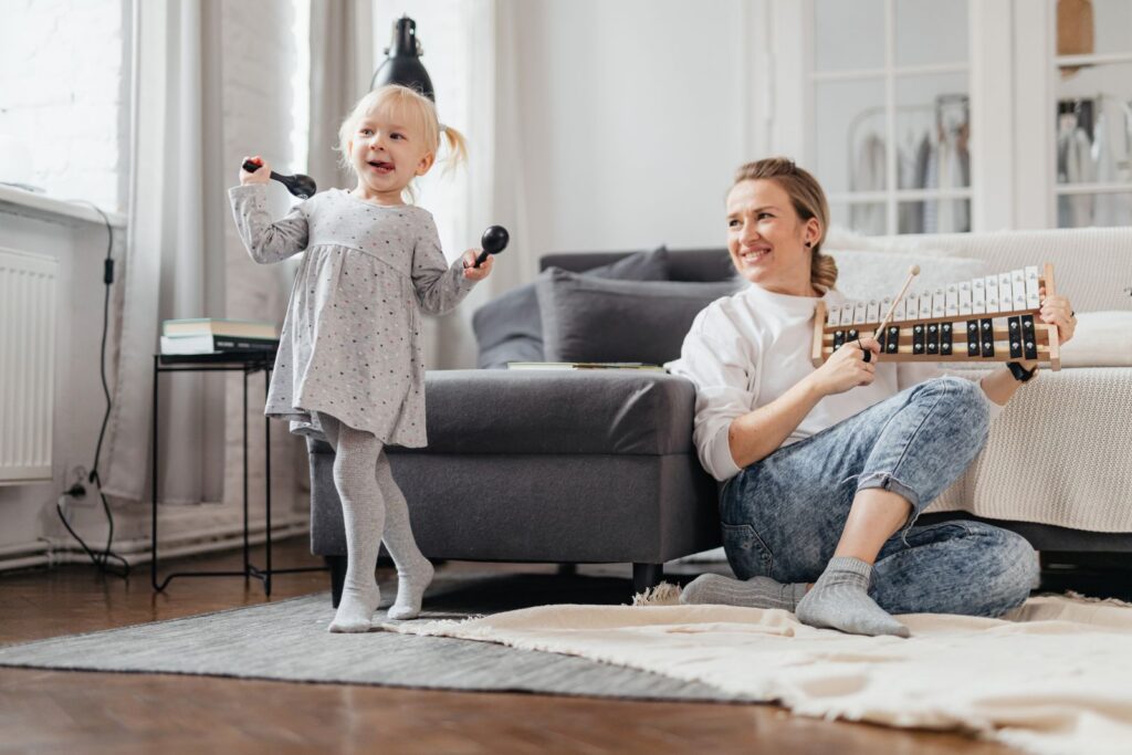 Preschool girl dancing with maracas while her mom plays a toy xylophone at home