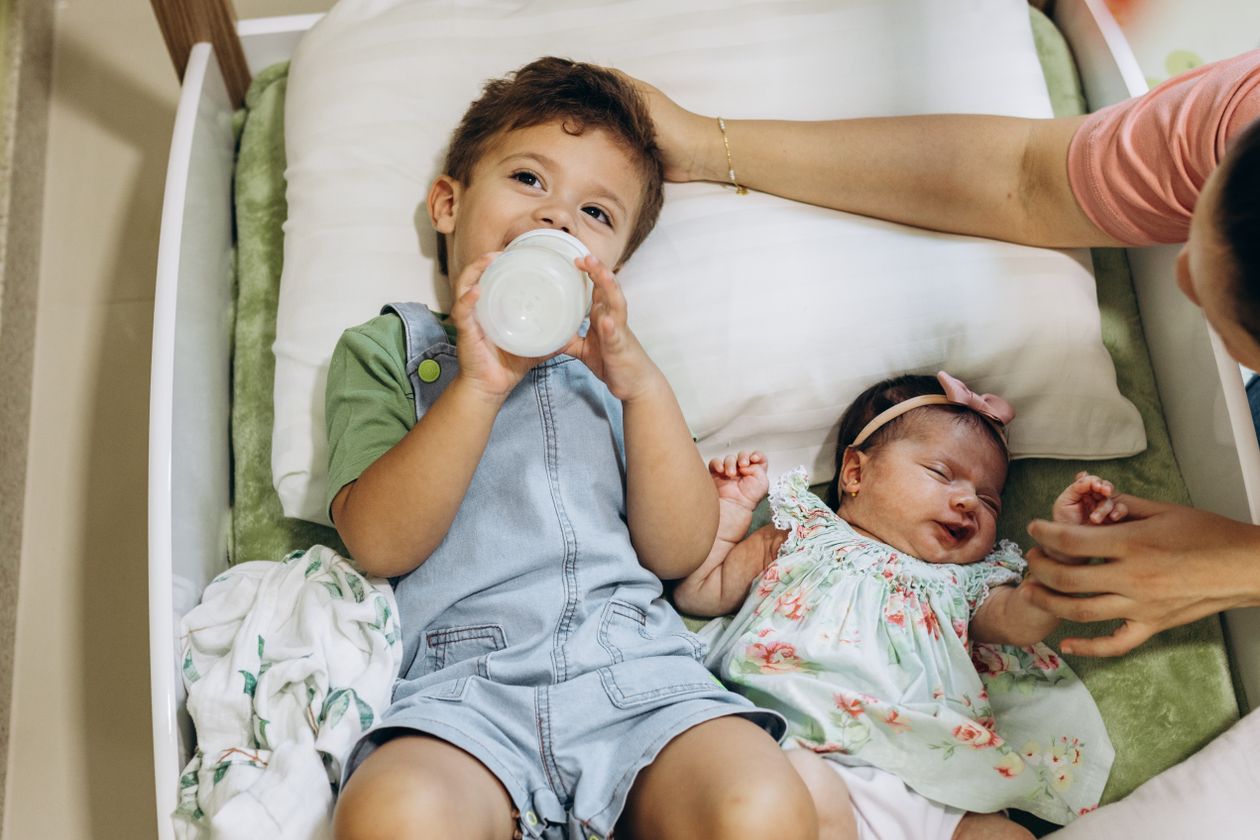 Mother's arms over son and baby in bed