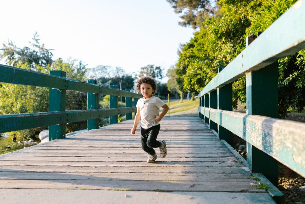 Toddler running across a wooden footbridge in a sunny park