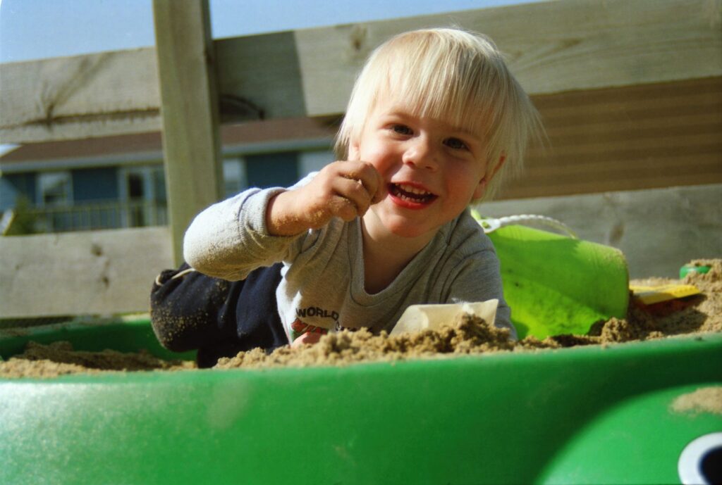 Smiling preschool boy playing in a sandbox, where early STEM skills show up in everyday play