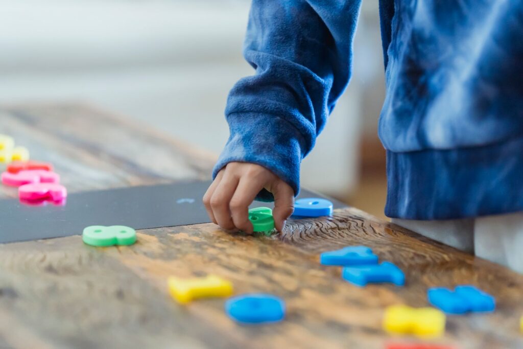 Preschooler lining up colorful toy numbers in rows on a wooden table