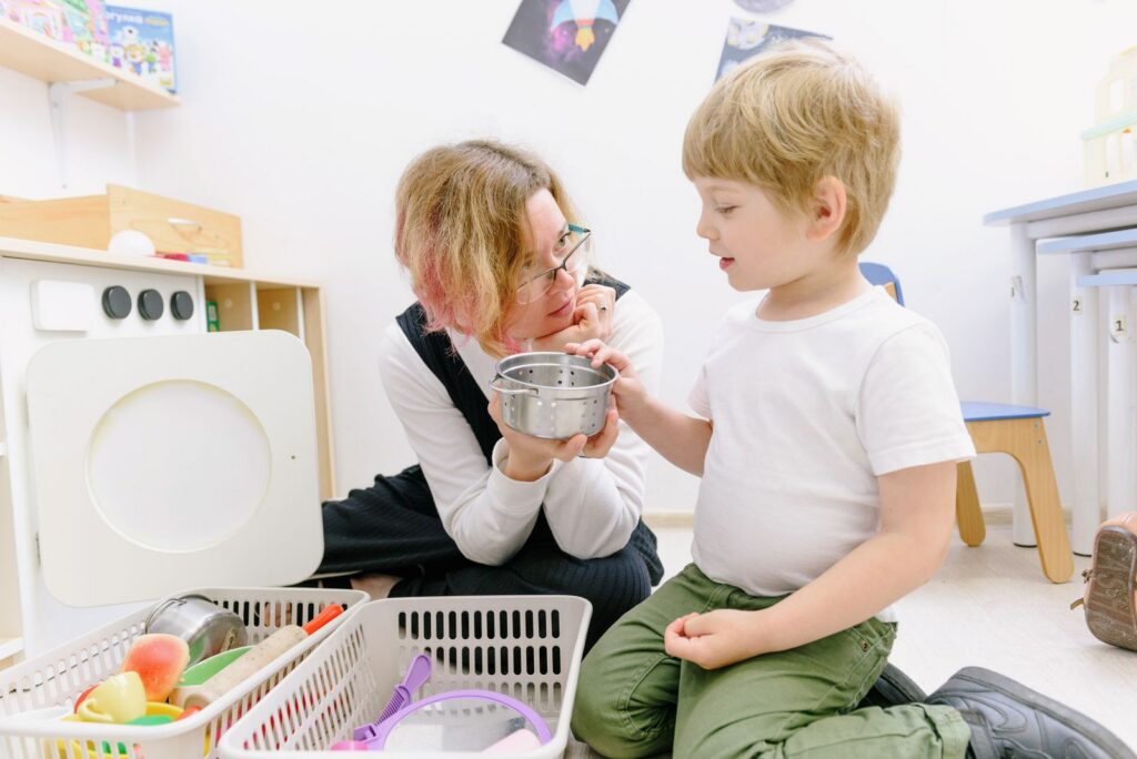 Preschool teacher kneeling with a young boy during play in a classroom