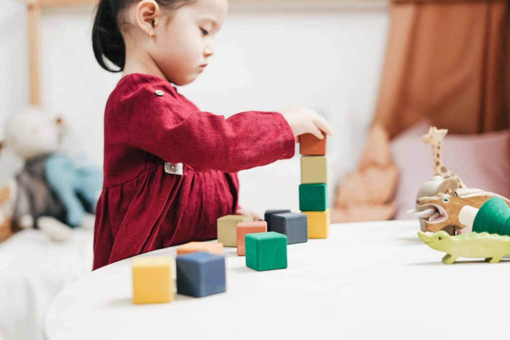 Preschool girl stacking a tower of colorful wooden blocks