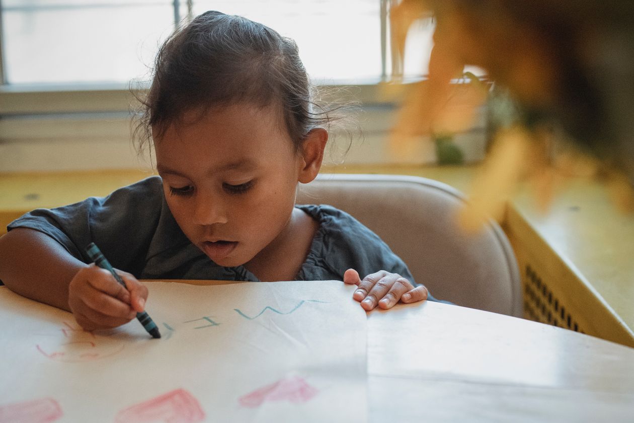 Focused preschool girl drawing with crayons at home