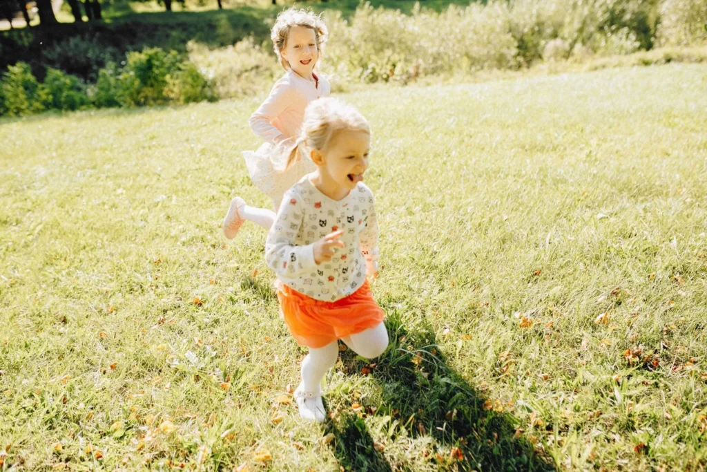 Two laughing toddlers running side by side across a sunny grass field
