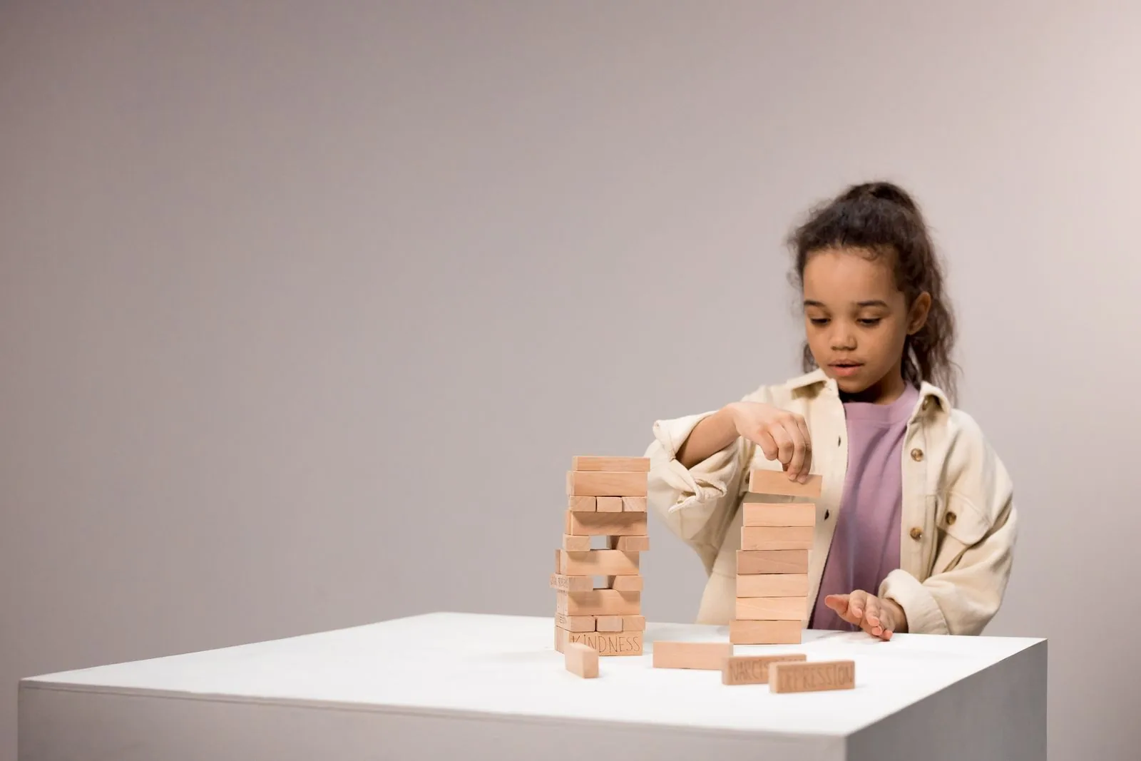 Young girl carefully stacking wooden blocks into a tower on a white table