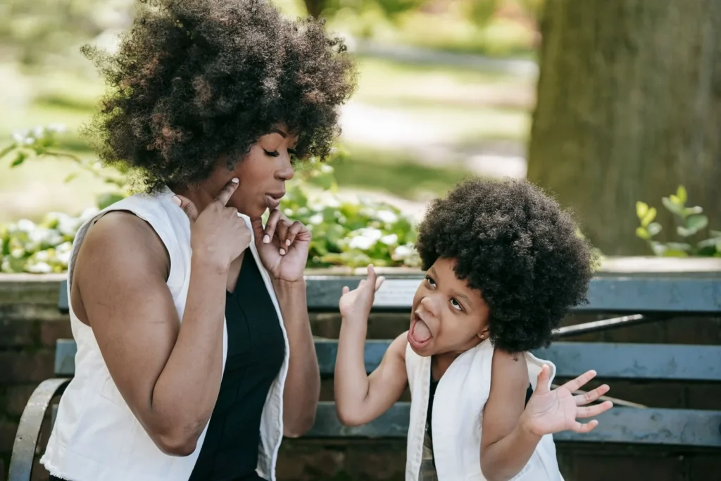 Mom with a finger on her chin and her preschooler shrugging on a park bench, both wondering