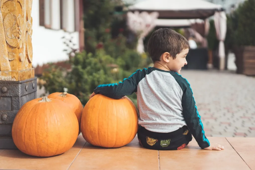 Young boy sitting on a porch step beside two big orange pumpkins