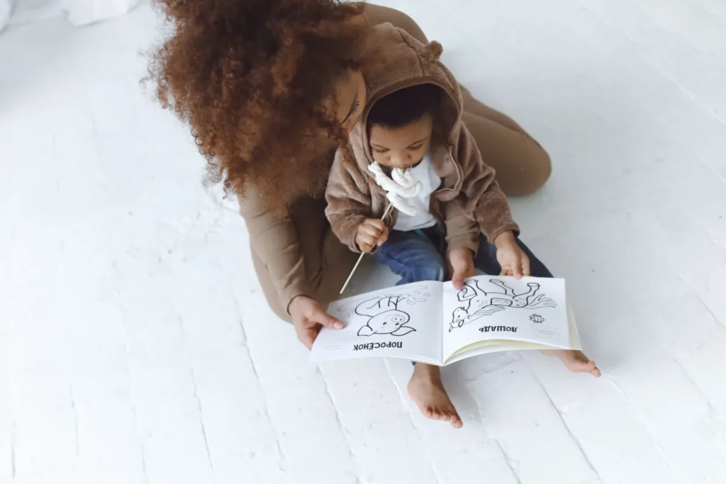 Mom and toddler sitting on a white floor looking at a picture book together