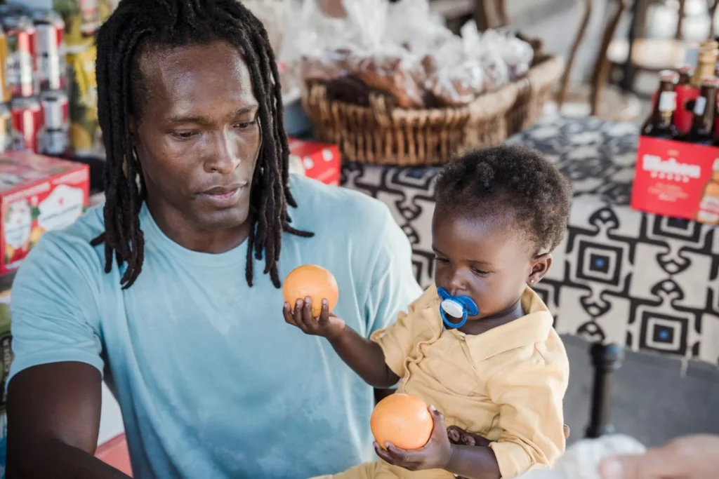 Dad and toddler each holding an orange at an outdoor market stall