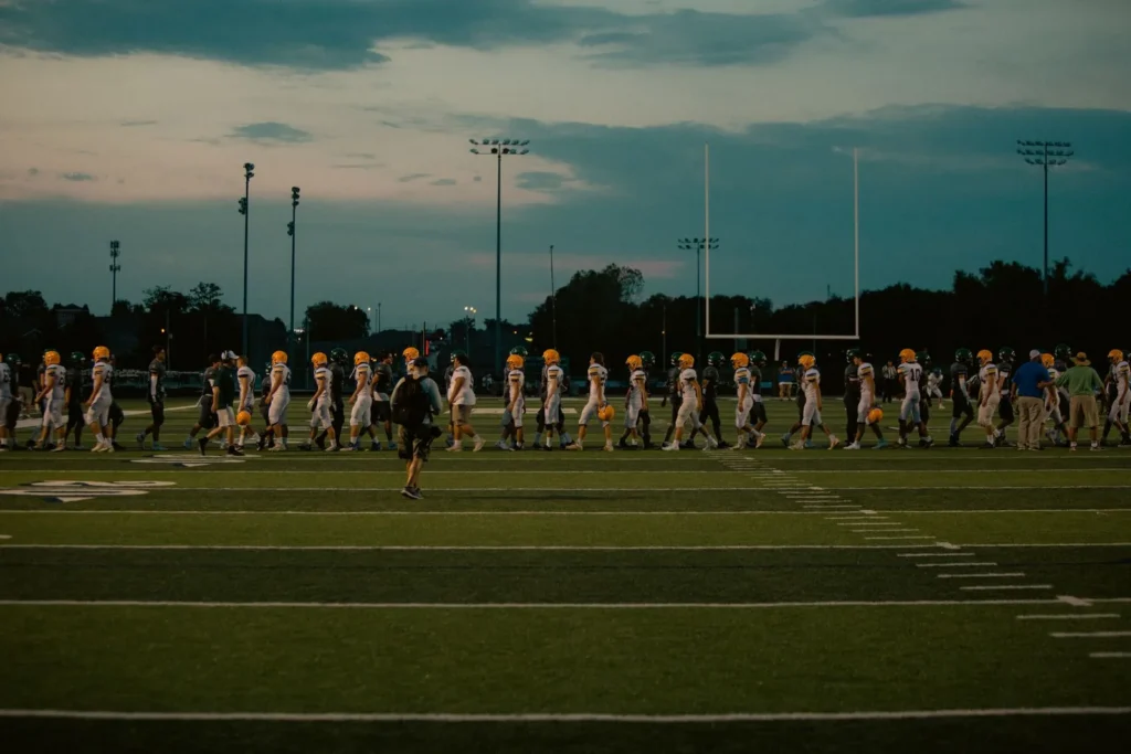 Football team walking across a stadium field under the lights at dusk on game night